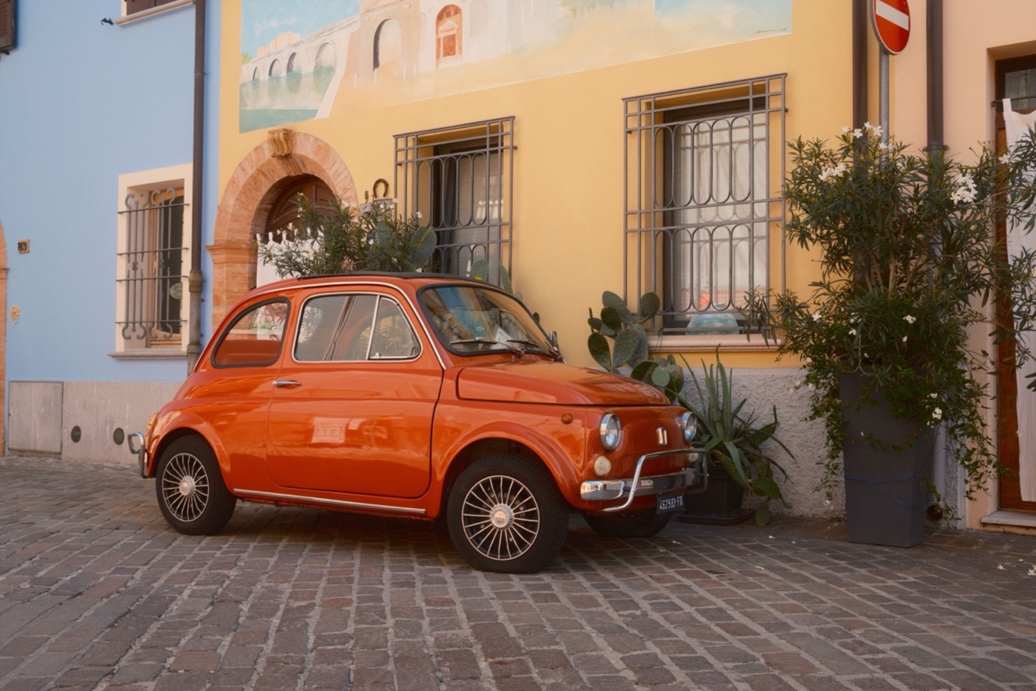 A small orange car parked on cobblestones in front of painted houses.