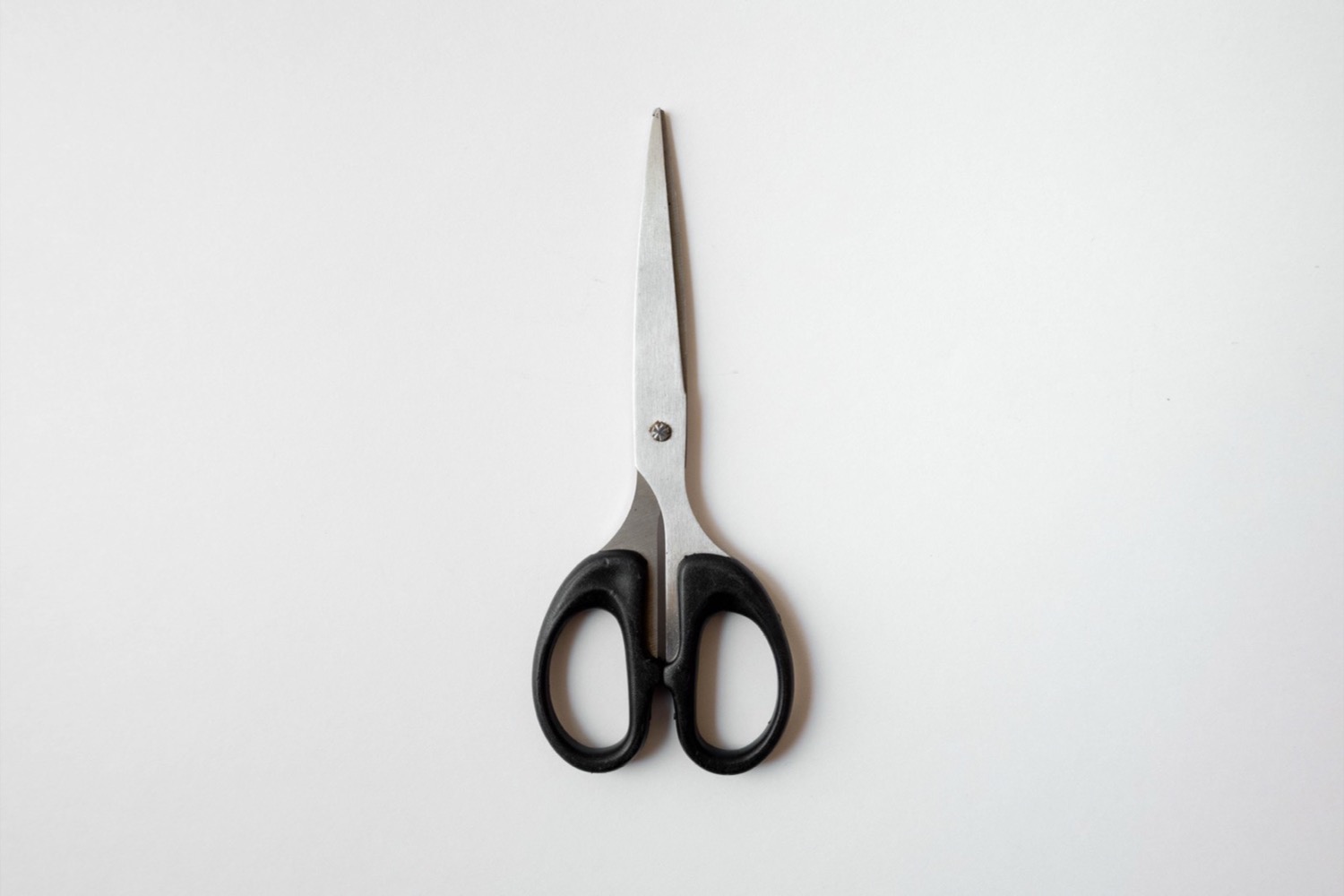 A pair of scissors lying on a plain pale surface.
